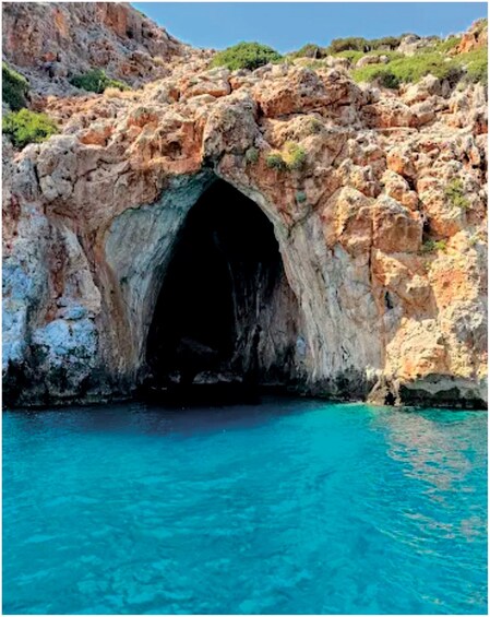 A rocky cave entrance with clear blue water below. 2