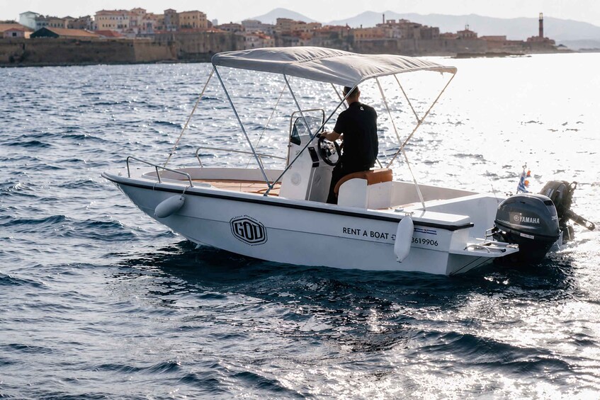 A white motorboat with a canopy, labeled 'GOD,' on a body of water with a coastal town and a lighthouse in the background. 1