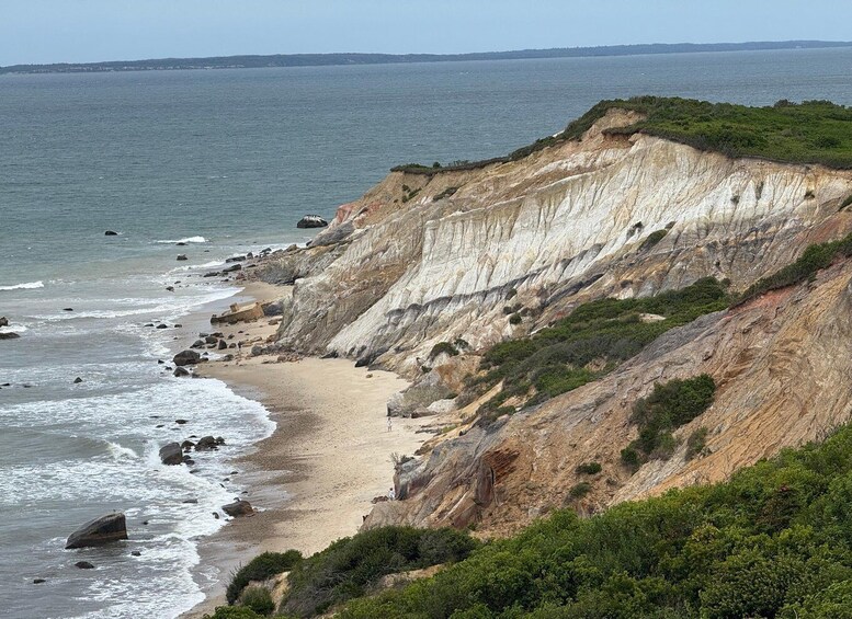 A coastal landscape with a sandy beach, steep cliffs, and a calm sea. 1