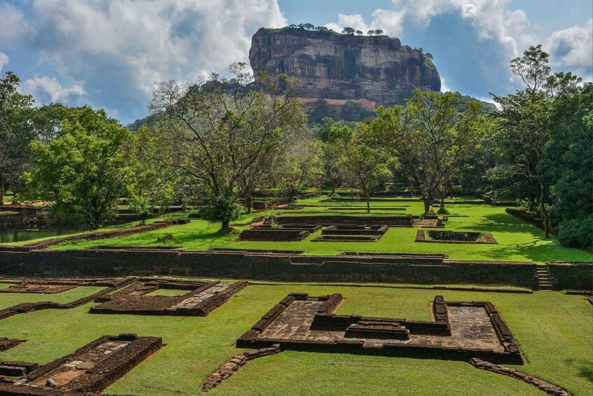 An archaeological site with terraced structures and a prominent rock formation in the background. 2