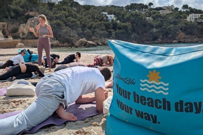 A group of people doing yoga on a beach with a blue mat that reads 'Nani Blue Your beach day Your way.' 5