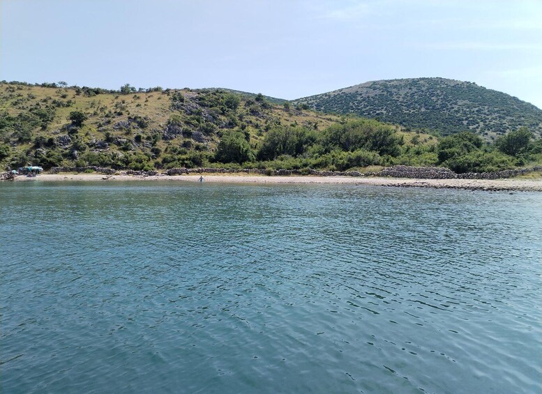 A calm lake with a rocky shoreline, surrounded by hills with sparse vegetation. 4