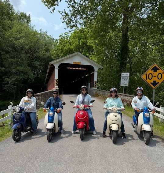 Five people on scooters in front of a covered bridge with a weight limit sign. 2