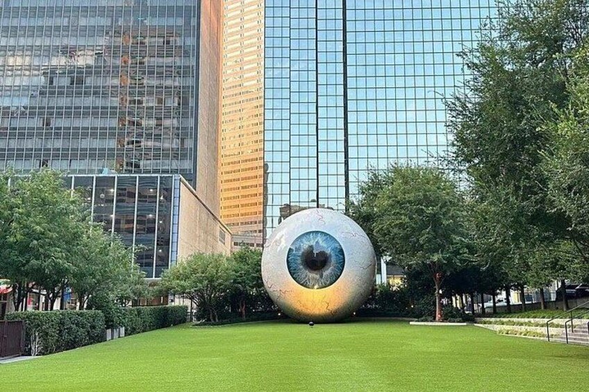 A large spherical sculpture in a park with modern buildings in the background. 2