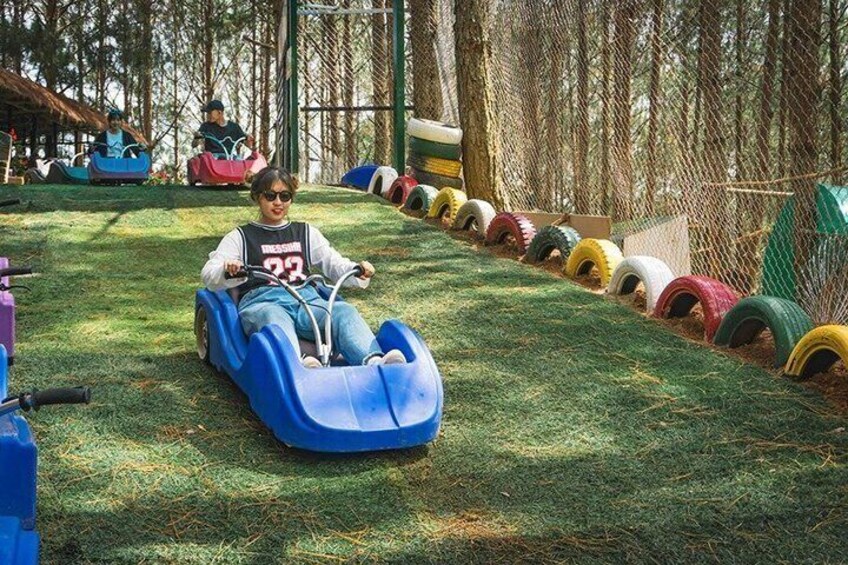 A person riding a blue bumper car on a grassy area with a fence and colorful tires in the background. 2