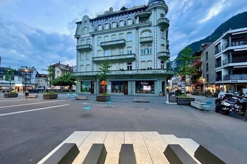 A historic building with ornate architecture, a pedestrian plaza with seating, and a crosswalk in a town square. 4