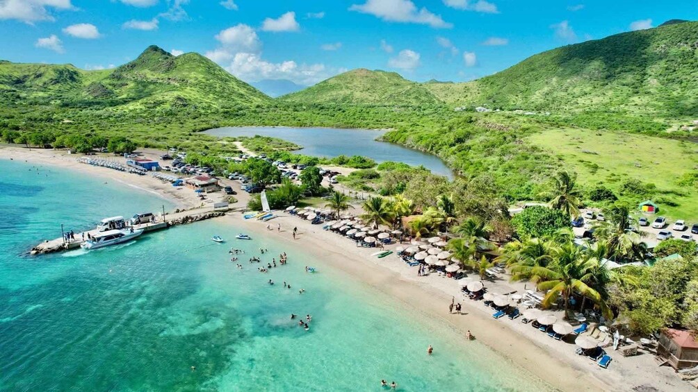 A tropical beach with clear turquoise waters, a dock with boats, and a resort area with umbrellas and palm trees. 2