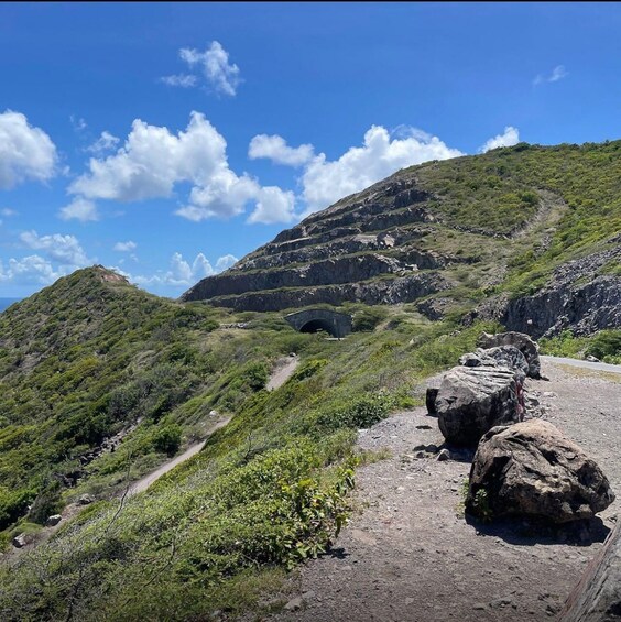A mountainous landscape with a dirt path, a tunnel, and large rocks. 3