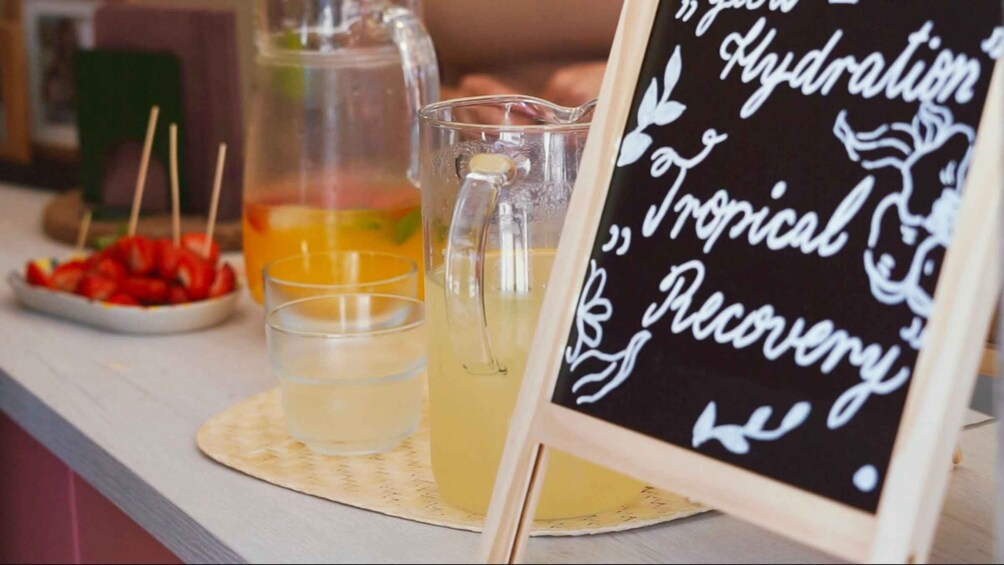 A beverage stand with a sign reading 'Hydration, Tropical Recovery,' and two glasses of a yellow drink. 4