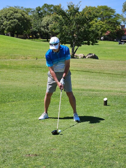 A man in a blue shirt and gray shorts preparing to put a golf ball on a green. 4