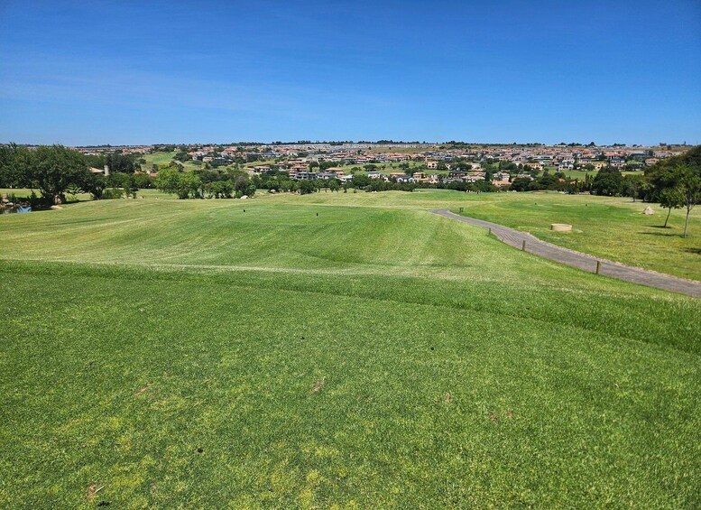 A grassy field with a path, a distant town, and a clear blue sky. 5