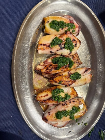 Grilled octopus with a green herb topping on a metal plate. 5