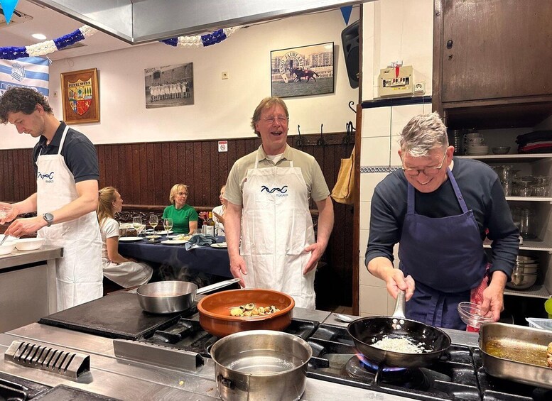 Chefs preparing food in a kitchen with a dining area visible in the background. 1