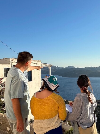 Three people standing by a building overlooking a body of water with mountains in the distance. 2