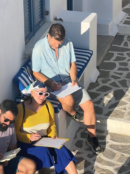 Three people sitting on a bench in a sunny outdoor setting with stone pavement. 3
