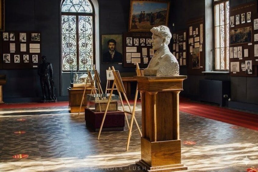 A museum interior with a bust on a pedestal, easels with paintings, and a statue in the background. 4