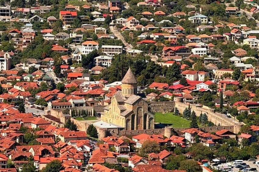 A densely populated town with red-roofed houses, a prominent church with a tall spire, and a fortified wall. 5