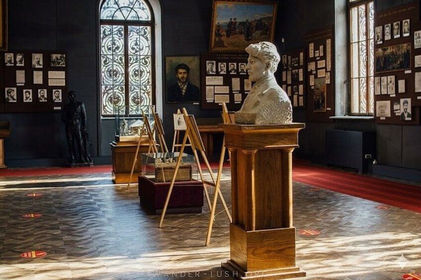 A museum interior with a bust on a pedestal, easels with paintings, and a statue in the background. 4