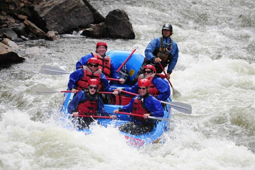 A group of people in a blue raft navigating a river with rapids. 3