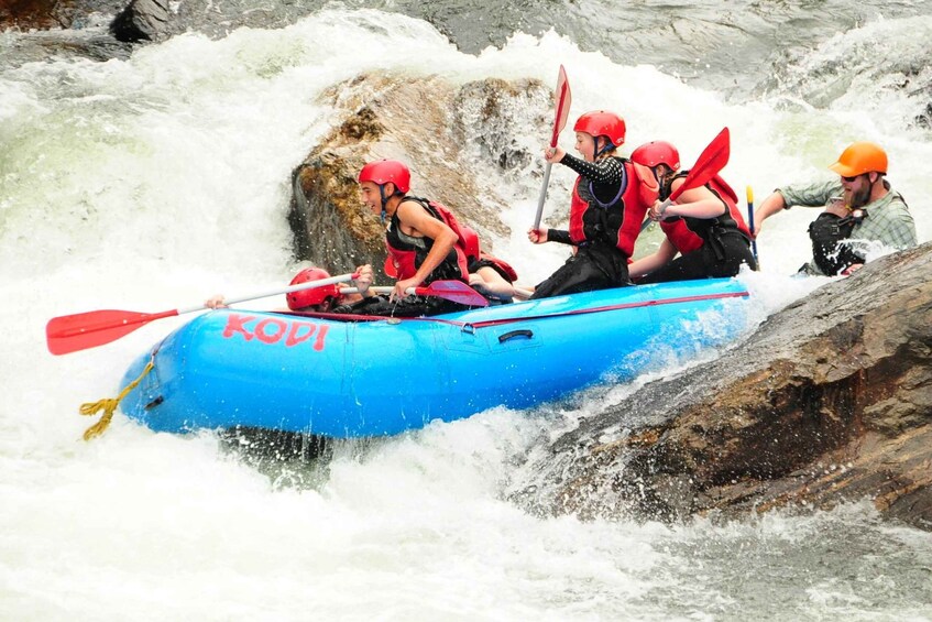 A group of people in a blue raft navigating a river with rapids. 1