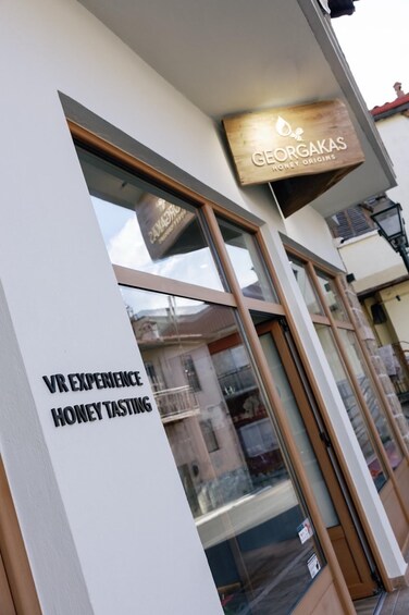 A storefront with a sign for 'VR EXPERIENCE HONEY TASTING' and another sign for 'GEORGAS GINGER ROOTS.' 5