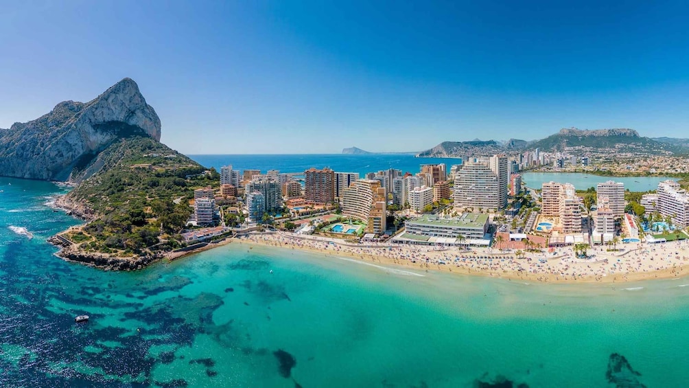 A coastal cityscape with a beach, high-rise buildings, and a prominent rocky outcrop. 1