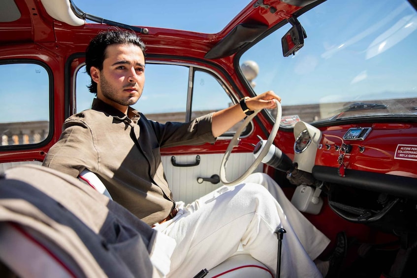 A person driving a red vintage car with a steering wheel and dashboard. 1