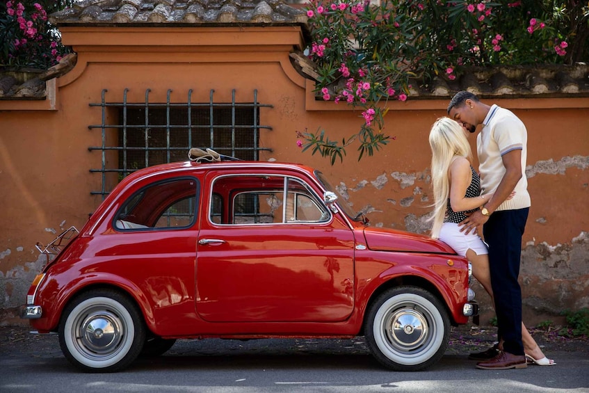 A red vintage car parked in front of a building with pink flowers and a metal gate. 1