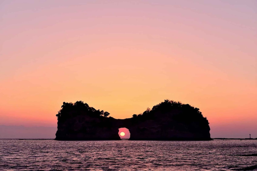 A sunset over a rock formation with water in the foreground. 1