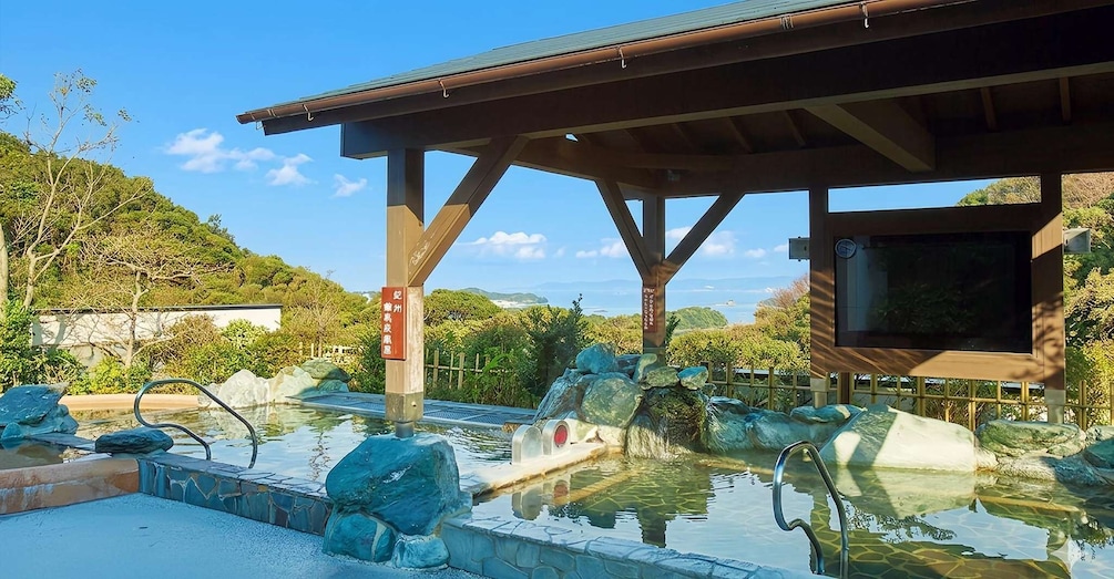 A traditional Japanese onsen with a wooden structure, a stone bath, and a view of the surrounding landscape. 3