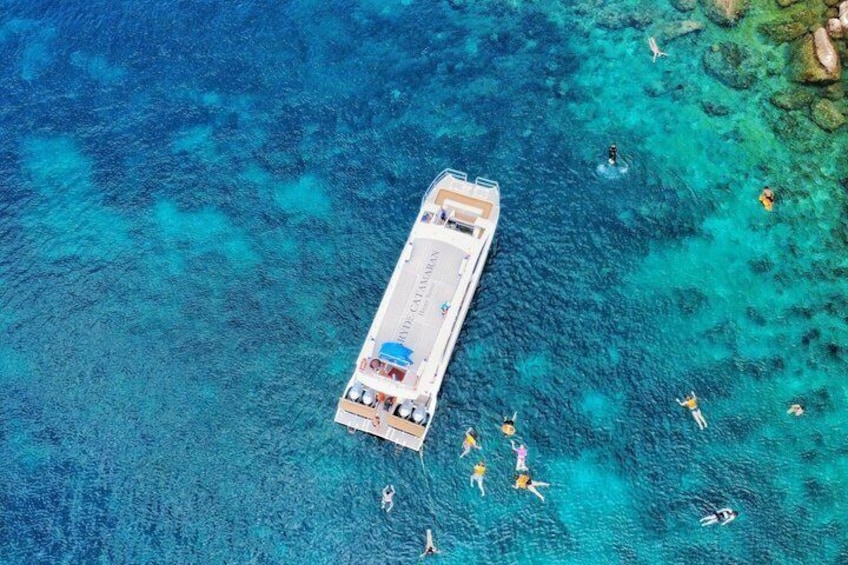 An aerial view of a pier with people swimming and sunbathing in clear turquoise waters. 1