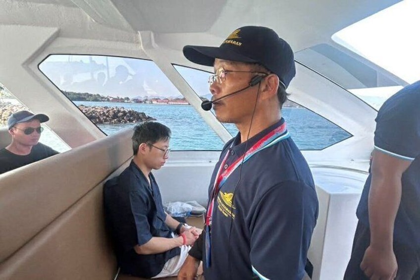 A boat interior with people, a view of the water, and a rocky shoreline in the background. 2