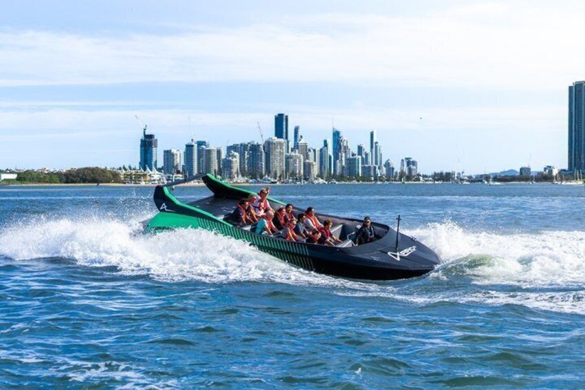 A speedboat with passengers on a body of water with a city skyline in the background. 1
