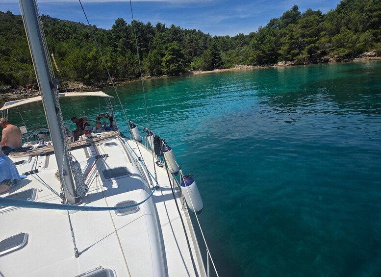 A sailboat on a turquoise sea with a forested coastline in the background. 1