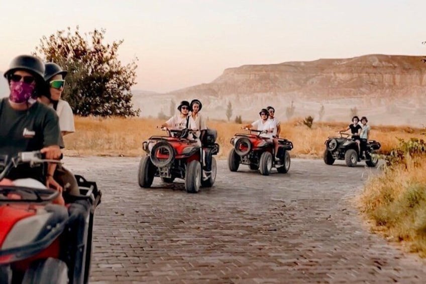 People riding ATVs on a paved road with a hilly landscape in the background. 4