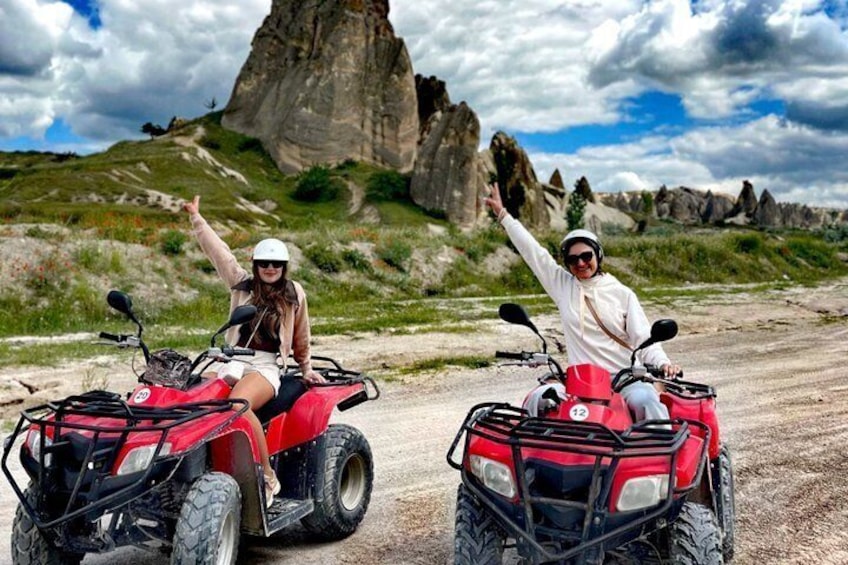 Two people on red ATVs on a dirt road with a large rock formation in the background. 1