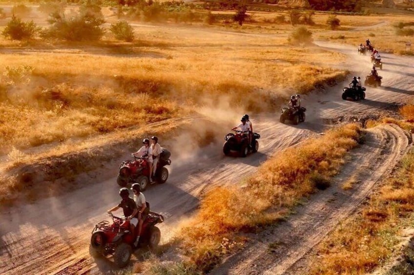 A group of riders on quad bikes on a dirt trail in a dry, grassy field. 5