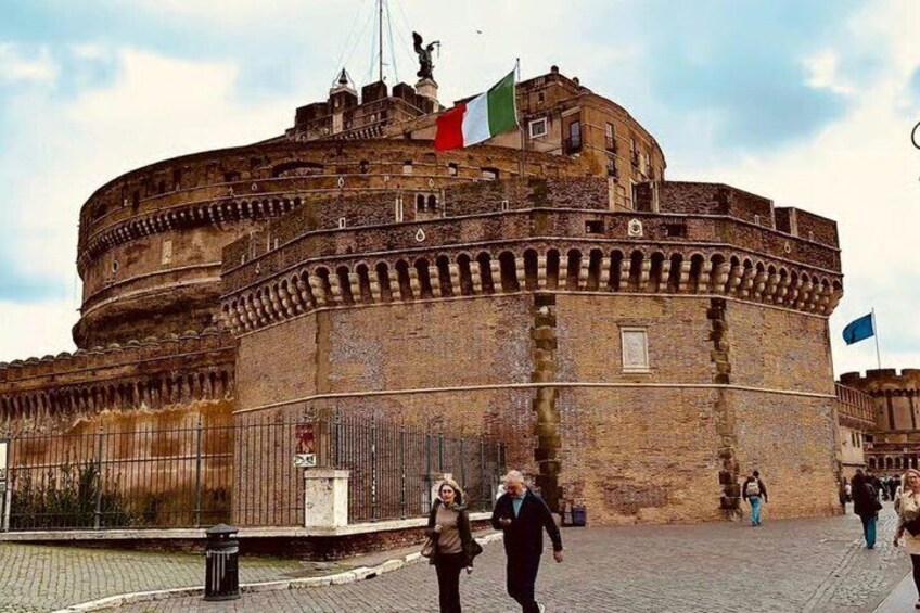 A historic stone fortress with a round tower, flags, and a cobblestone street. 1