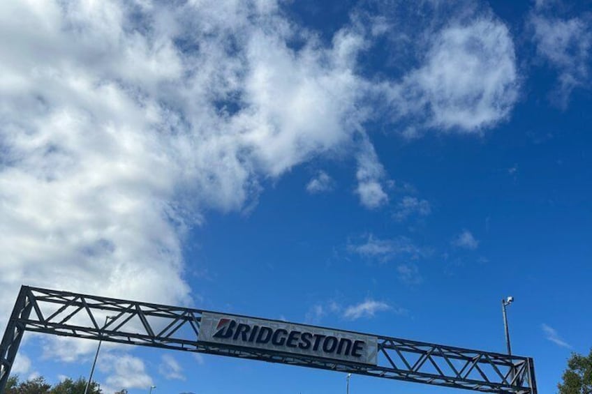 A metal bridge structure with the inscription 'BRIDGESTONE' against a blue sky with scattered clouds. 3