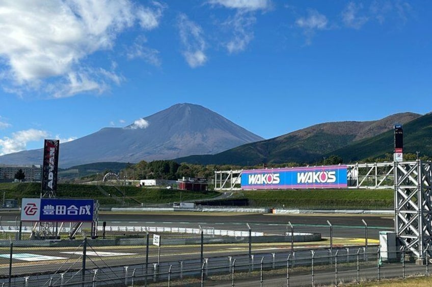 A racetrack with a mountain in the background, a blue sign with 'WAKOS' on it, and a sign with Japanese characters. 5