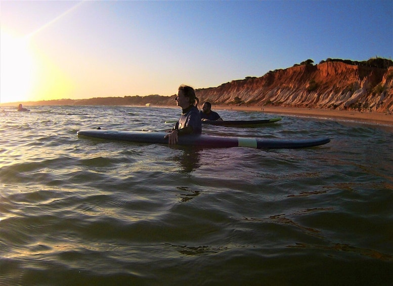 Two people sitting on surfboards in calm ocean waters with a rocky cliff in the background. 4