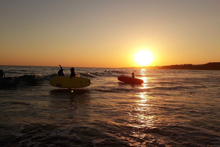 A sunset over a beach with people surfing and paddling on the water. 2