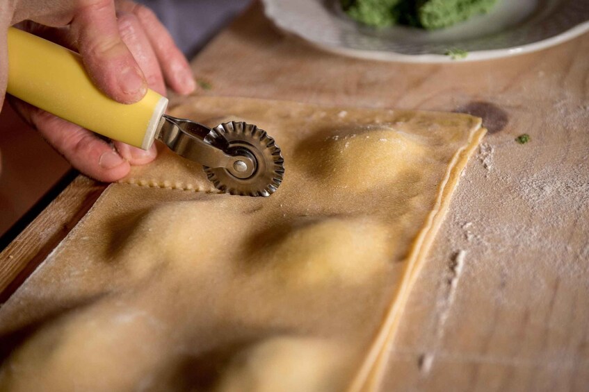 A person using a pasta cutter on a sheet of dough. 4