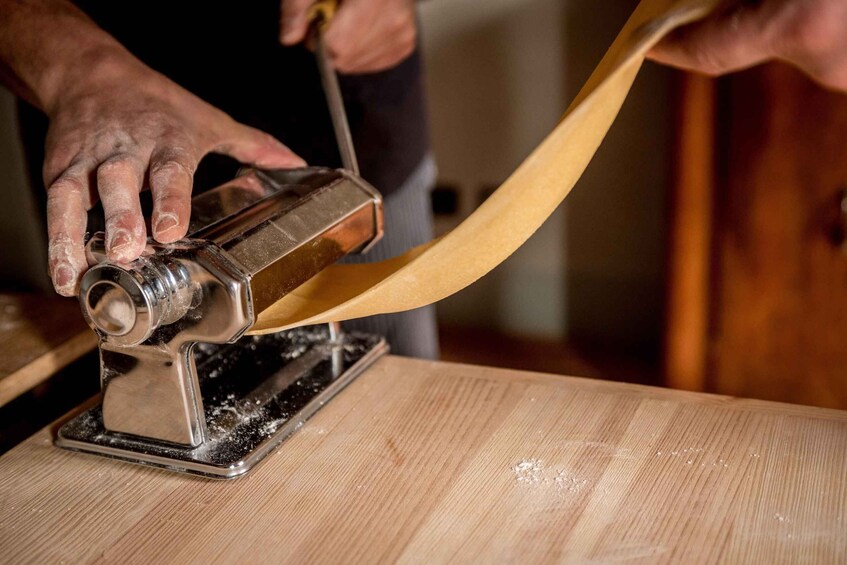 A person using a metal tool to shape a long, thin material on a wooden surface. 3