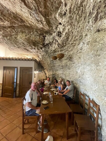 A group of people dining in a cave-like setting with stone walls and a tiled floor. 4