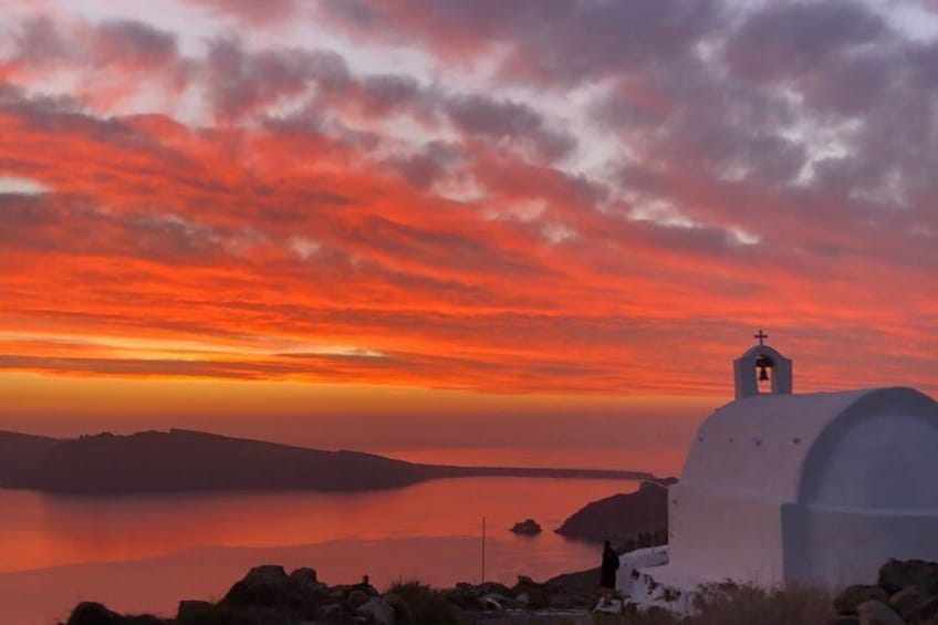 A white church with a bell tower on a hill overlooking a calm body of water during sunset. 2