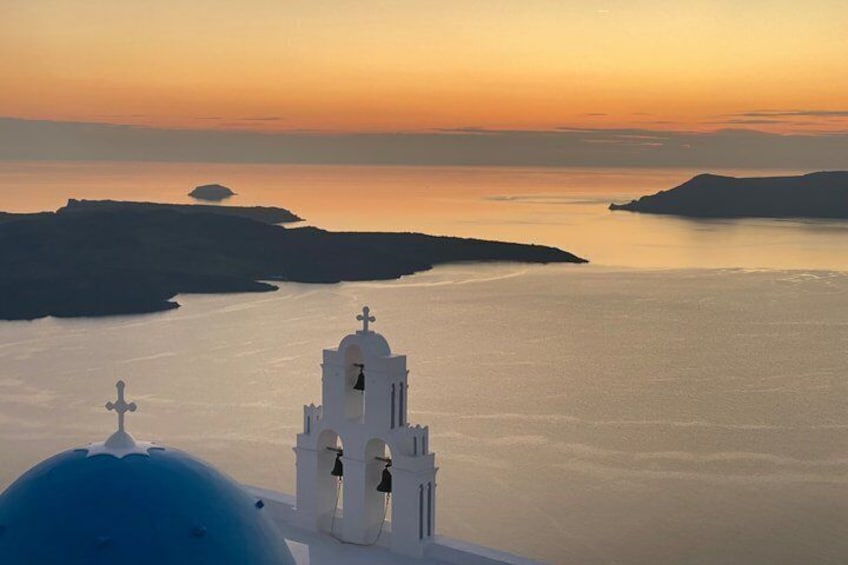 A white church with a blue dome and bell tower, overlooking a calm sea with distant islands. 1