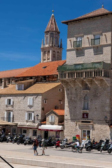 A historic town square with stone buildings, a church tower, and parked motorcycles. 3
