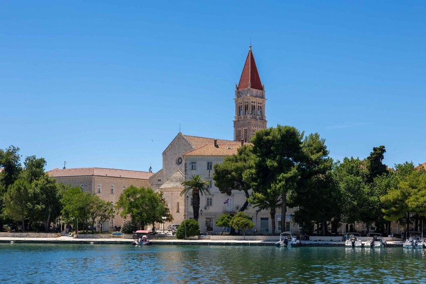 A historic building with a prominent tower, a calm waterfront, and lush green trees. 5