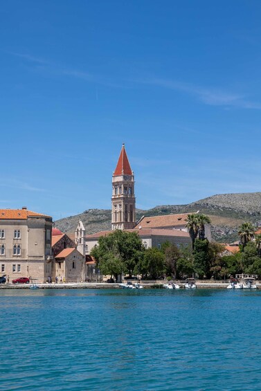 A coastal town with a prominent tower, calm sea, and hilly backdrop. 1